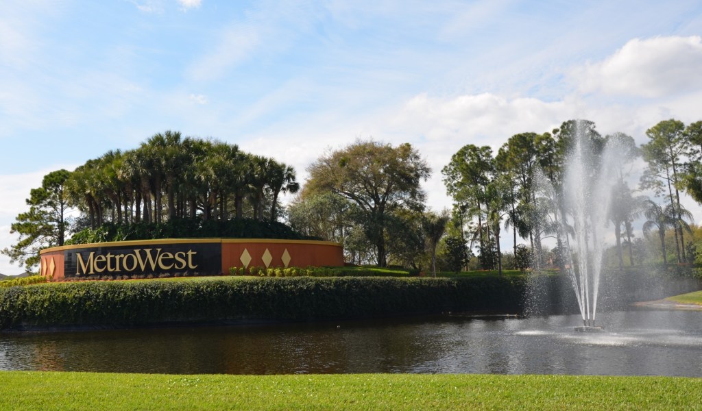 Welcome sign with decorative fountain and pond at entrance to commercial/medical complex, surrounded by palm trees and landscaping