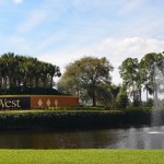 Welcome sign with decorative fountain and pond at entrance to commercial/medical complex, surrounded by palm trees and landscaping