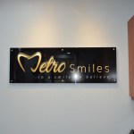 Metro Smiles clinic sign with gold heart logo on textured wall