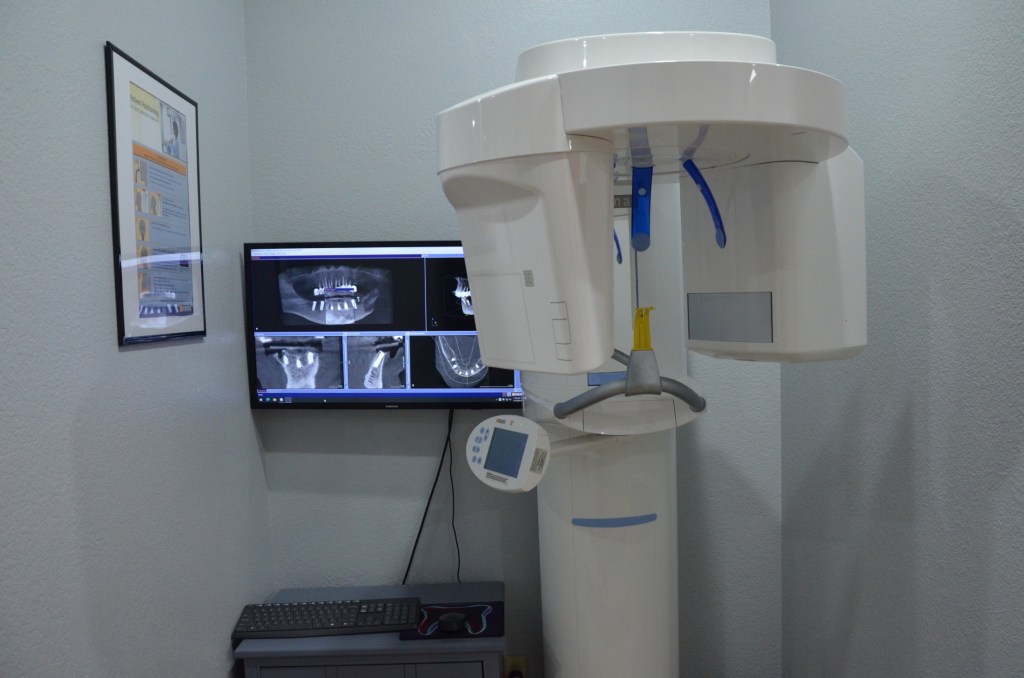 Dental panoramic X-ray room with imaging equipment and monitor displaying radiographs on gray wall