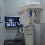 Dental panoramic X-ray room with imaging equipment and monitor displaying radiographs on gray wall