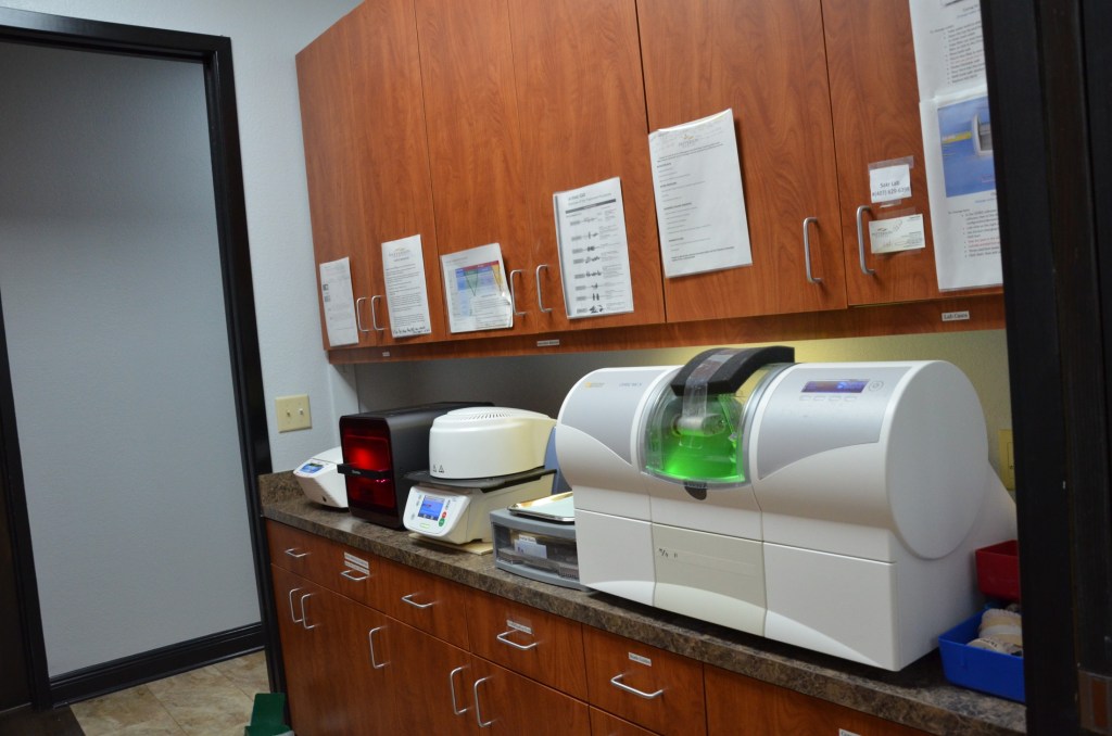 Dental lab workspace with wooden cabinetry and CAD/CAM milling machine for restorations