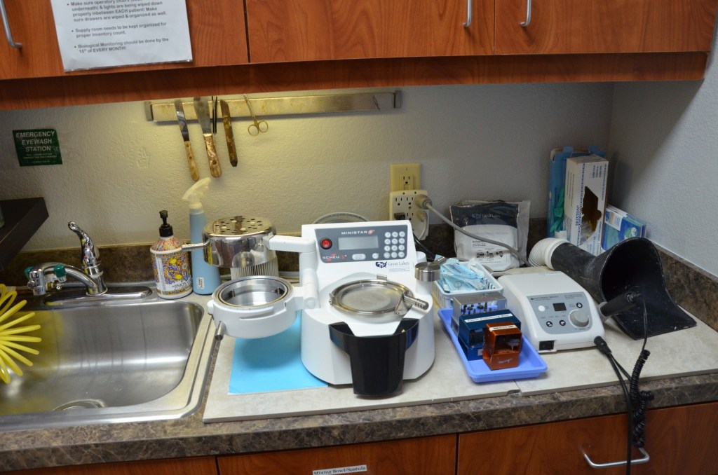 Dental lab workstation with sink, instruments, mixing equipment, and various laboratory supplies
