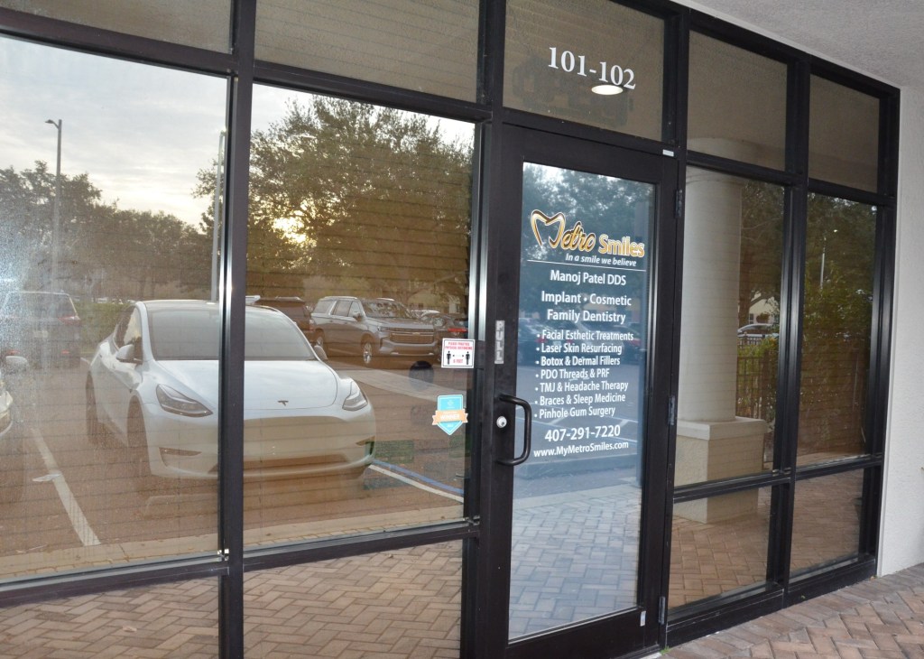 Glass entrance doors to medical/dental office building with reflections of parking lot and landscaping