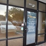 Glass entrance doors to medical/dental office building with reflections of parking lot and landscaping
