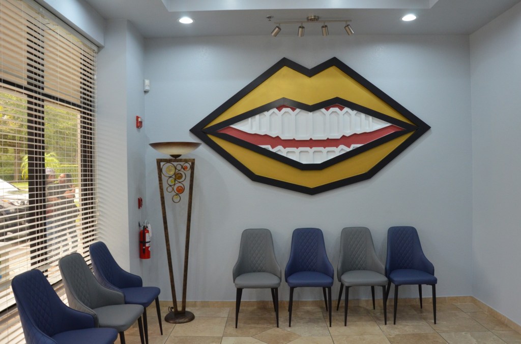 Modern dental office waiting room with blue chairs, decorative lip artwork on wall, and contemporary design